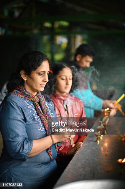 mother and daughter praying by holding lighted incense sticks in their hand - temple body part stock pictures, royalty-free photos & images