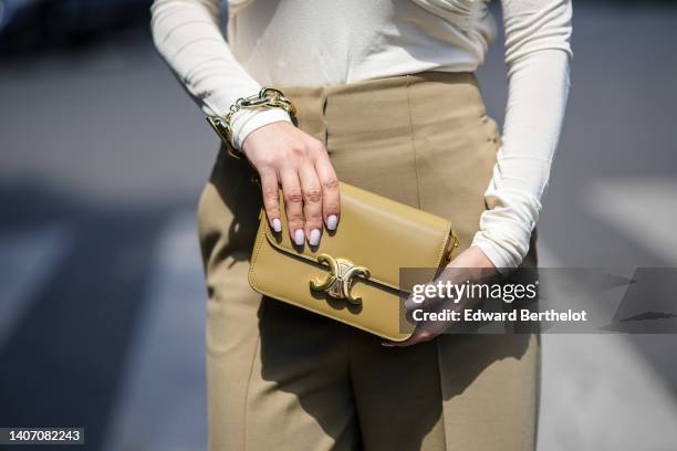 Justyna Czerniak wears a white latte V-neck / shoulder-off / long sleeves body, high waist beige wide legs pants, a beige shiny leather clutch from...