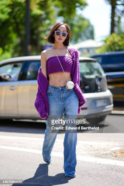 Chriselle Lim wears purple sunglasses, silver earrings, a white shiny leather circle crossbody bag from Chanel, a neon purple braided wool...