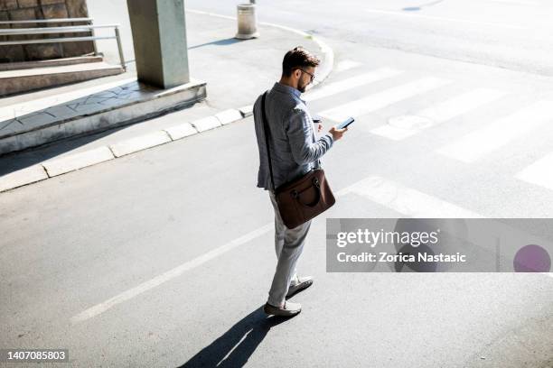 uomo d'affari fiducioso che passa per strada usando il telefono - borsa per laptop foto e immagini stock