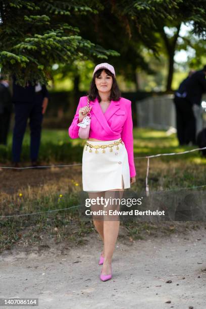 Clervie Rose wears a white with pink checkered print pattern tweed cap from Chanel, gold earrings, a neon pink cropped blazer jacket, a pink shiny...