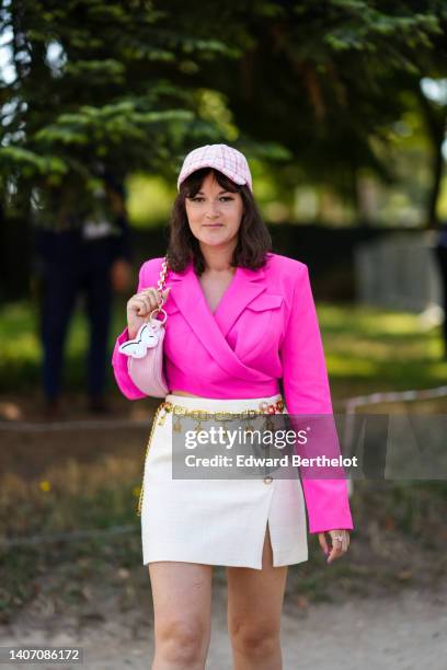 Clervie Rose wears a white with pink checkered print pattern tweed cap from Chanel, gold earrings, a neon pink cropped blazer jacket, a pink shiny...