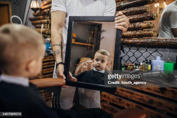 barbero mostrando corte de pelo a un niño pequeño también lo ve en el espejo en la barbería - barber shop fotografías e imágenes de stock