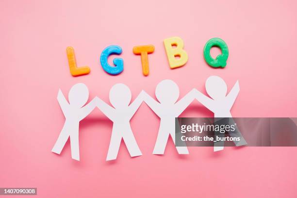 high angle view of paper people with arms raised and colorful lgbtq letters on pink background - chain link stock pictures, royalty-free photos & images