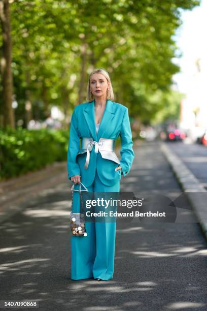 Justyna Czerniak wears gold earrings, a pale blue oversized blazer jacket, matching blue suit pants, a silver metal-disc shoulder bag from Paco...