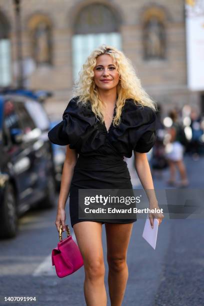 Pixie Lott wears a black short puffy sleeves / V-neck / short tube dress, a neon pink shiny leather handbag from Schiaparelli, outside the...