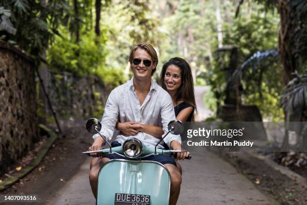young couple riding classic scooter during vacation in bali - tourist couple fotografías e imágenes de stock