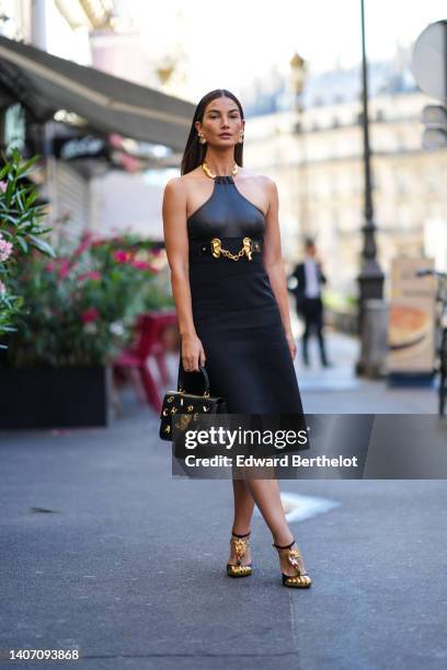 Lily Aldridge wears gold earrings from Schiaparelli, a black shiny leather halter neck / gold necklace top from Schiaparelli, a black high waist /...