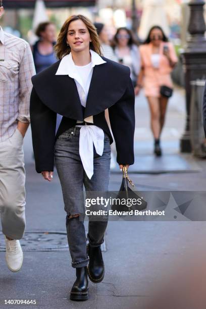 Emma Watson wears a white t-shirt, a white oversized / cropped shirt, a black oversized epaulets / shoulder-pads cropped jacket, gray denim ripped...