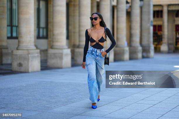 Emilie Joseph wears black sunglasses, a black shiny grained leather Boy shoulder bag from Chanel, a black Cut out dress worn as a dress from Amazuin...