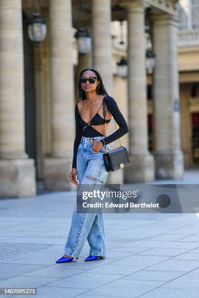 Emilie Joseph wears black sunglasses, a black shiny grained leather Boy shoulder bag from Chanel, a black Cut out dress worn as a dress from Amazuin...