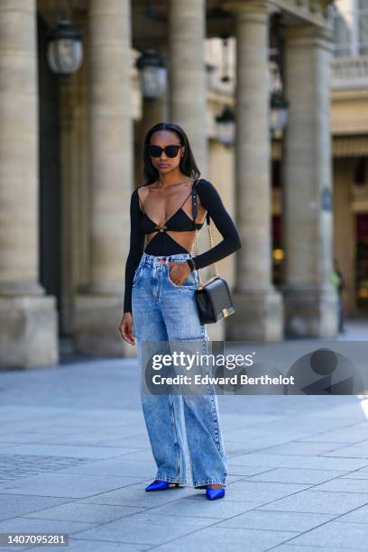 Emilie Joseph wears black sunglasses, a black shiny grained leather Boy shoulder bag from Chanel, a black Cut out dress worn as a dress from Amazuin...