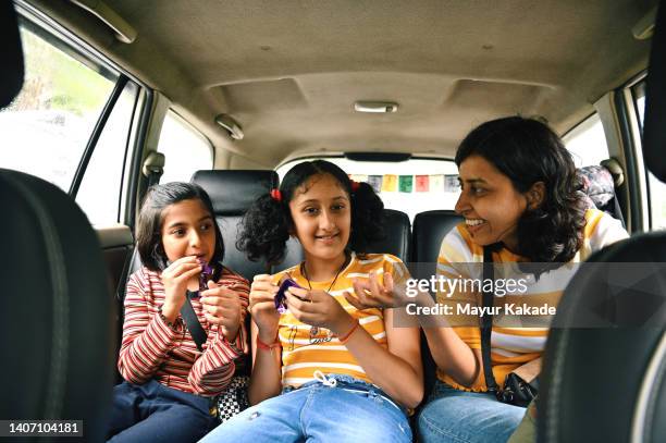 mother and daughters eating chocolate and enjoying their time sitting inside the car while travelling - sharing chocolate stock-fotos und bilder