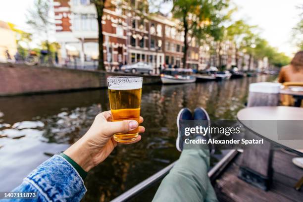 man relaxing and drinking beer by the canal in amsterdam, personal perspective view, netherlands - beer flowing stock pictures, royalty-free photos & images