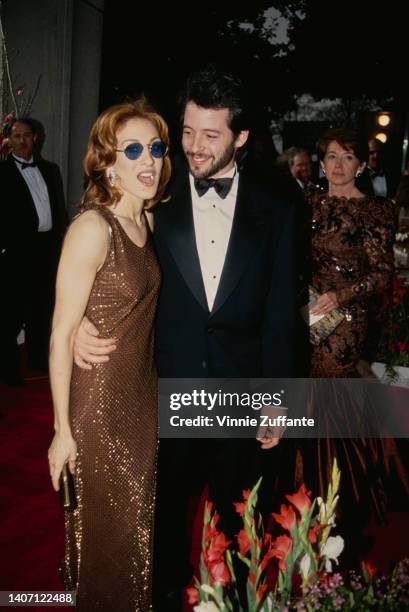 American actress Sarah Jessica Parker, wearing a bronze-coloured dress and blue sunglasses, and American actor Matthew Broderick, wearing a tuxedo...