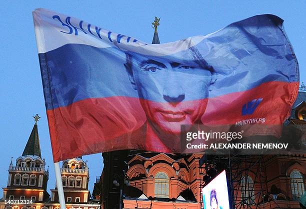 Russian flag featuring Prime Minister Vladimir Putin flies above his supporters as they celebrate Putin's victory as they rally at the central...