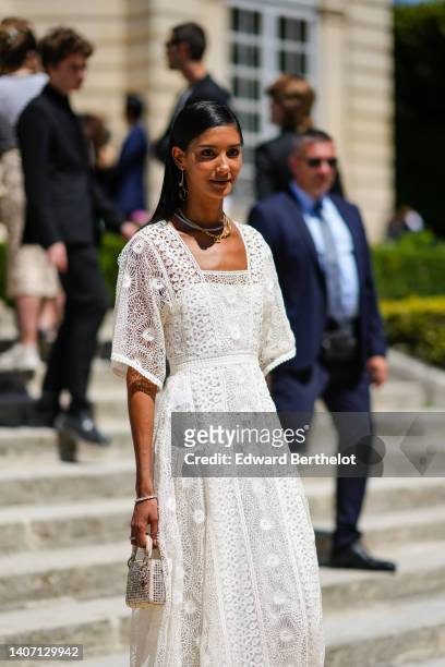 Guest wears gold pendant earrings, a gold chain necklace from Dior, a silver necklace, a white lace pattern short sleeves / belted long dress, a...