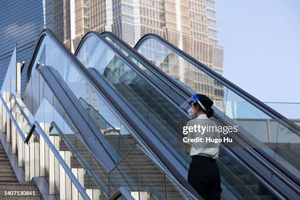 Security woman with protective mask takes an escalator at Lujiazui on July 06, 2022 in Shanghai, China.