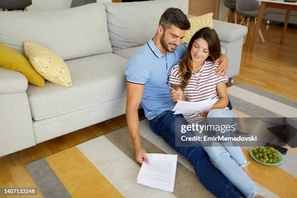 mid adult couple sitting together on carpet in living room and checking their finances - demonstration against the marriage for all bill stock pictures, royalty-free photos & images