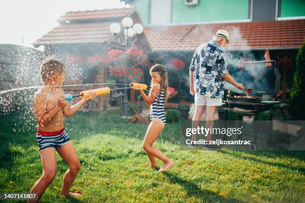 abuelo y nieto están haciendo una barbacoa en el patio trasero y salpicándose el uno al otro con agua d - water garden fotografías e imágenes de stock