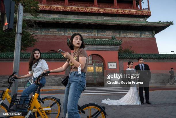 Two women stop on their shared bikes in front of a couple who were having their pre-wedding photos taken in front of the Drum Tower in a hutong...