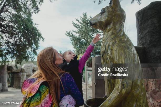little girl upa from her mother stretching out her arm trying to touch a giant wooden kangaroo - cordoba argentina ストックフォトと画像