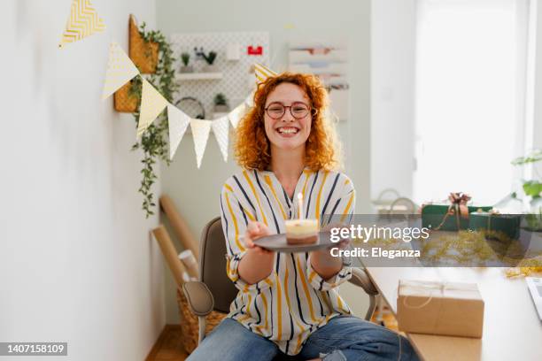 beautiful young woman celebrating birthday in her office - birthday hat stock pictures, royalty-free photos & images