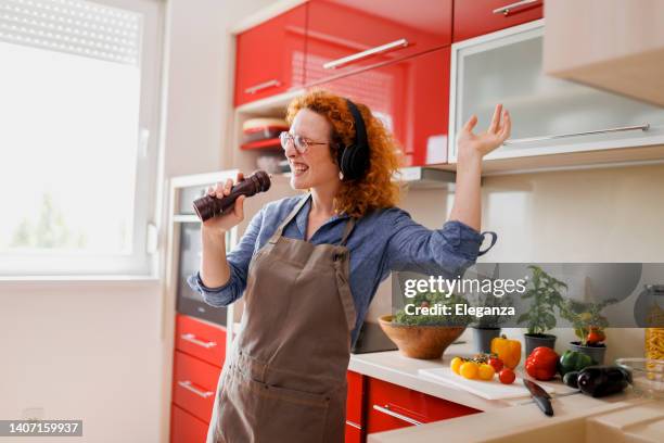 mujer sonriente escuchando música y bailando en la cocina - melody maker fotografías e imágenes de stock