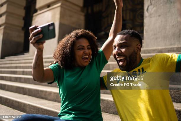 brazilian fans watching soccer game using mobile phone outdoors - football phone stock pictures, royalty-free photos & images