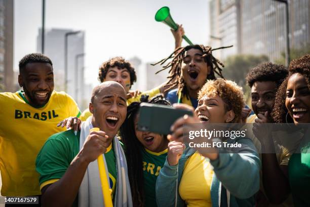 brazilian fans watching soccer game using mobile phone outdoors - fifa world cup fans stock pictures, royalty-free photos & images