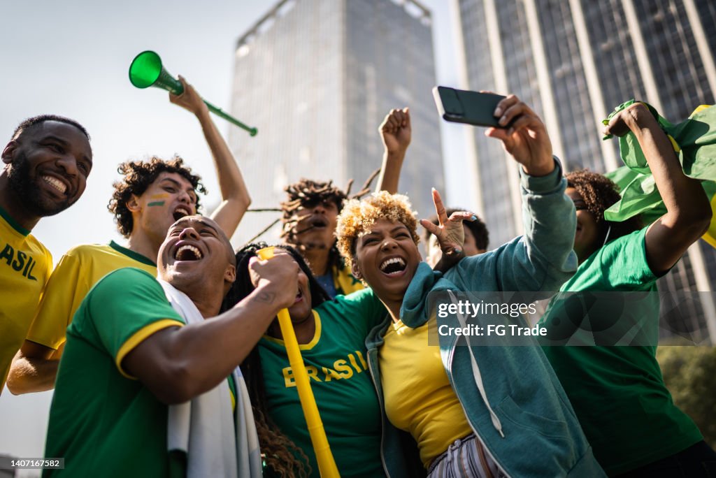 Brazilian fans watching soccer game using mobile phone outdoors