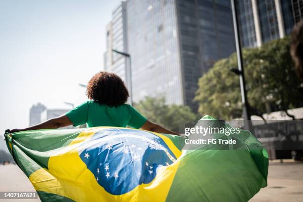 fan brasiliani che camminano e tengono una bandiera brasiliana sulla città - brazilian flag foto e immagini stock
