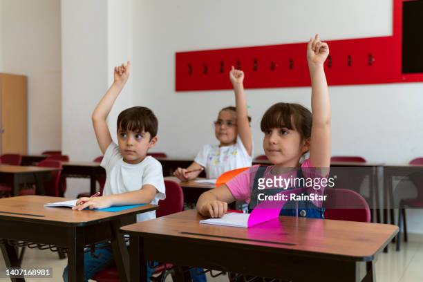 shot of a diverse group of children sitting in their school classroom and raising their hands to answer a question - turkey school stockfoto's en -beelden