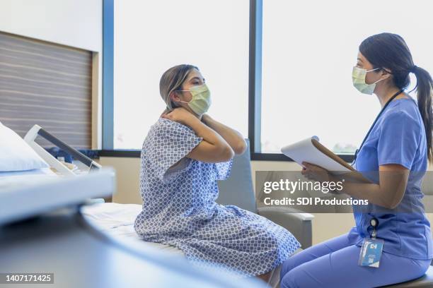 female patient in hospital gown shares symptoms with doctor - hospital gown imagens e fotografias de stock