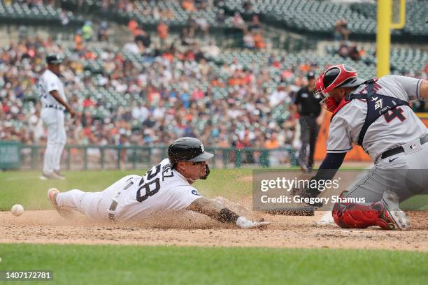 Javier Baez of the Detroit Tigers slides into home plate past Sandy Leon of the Cleveland Guardians to score a fifth inning run at Comerica Park on...