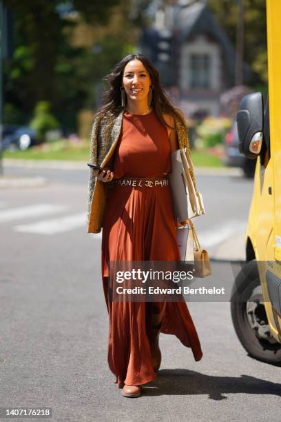 Guest wears gold logo and fringed pendant earrings from Chanel, gold bracelet, a beige with embroidered blue and brown tweed jacket, a red brown...