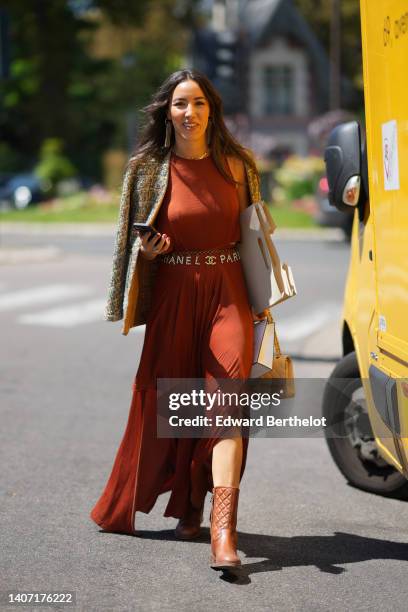 Guest wears gold logo and fringed pendant earrings from Chanel, gold bracelet, a beige with embroidered blue and brown tweed jacket, a red brown...
