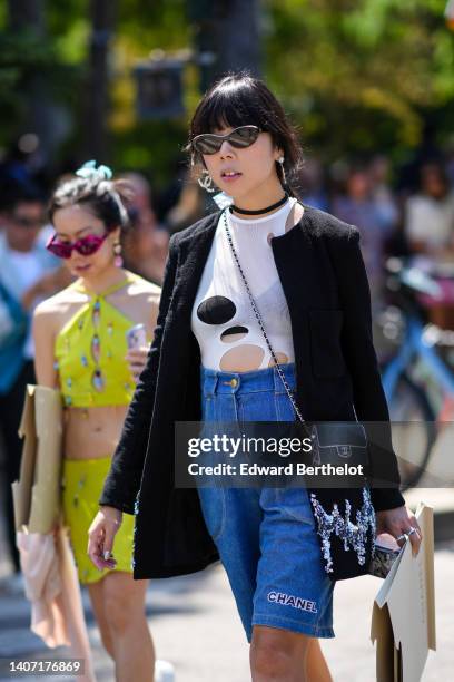 Guest wears black sunglasses from Chanel, rhinestones logo pendant earrings from Chanel, a black necklace, a black long jacket, a white ripped body,...