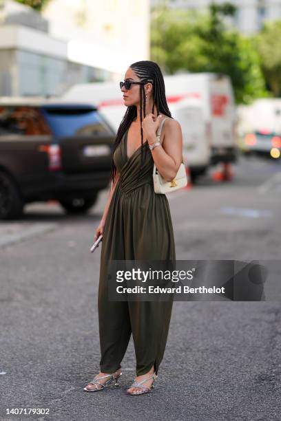 Guest wears black sunglasses from Celine, silver earrings, a khaki wrap V-neck / puffy jumpsuit, a white latte matte leather shoulder bag from...
