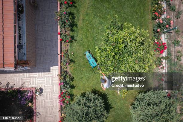 aerial view of woman mowing grass at backyard with an electric mower - handgrasmaaier stockfoto's en -beelden