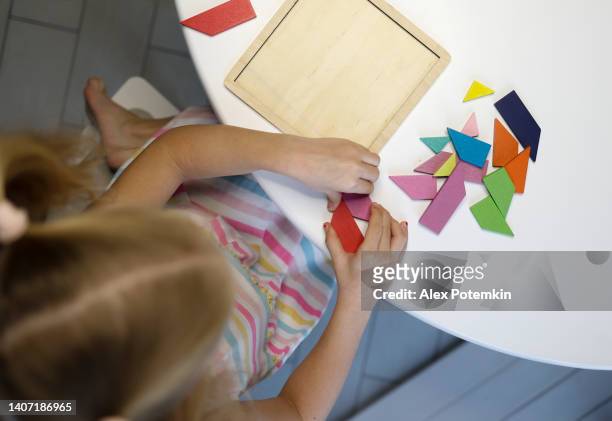 kleines mädchen, das mit einem tangram-puzzle spielt. direkt über der ansicht, selektiver fokus auf hände und puzzle mit defokussiertem vordergrund. - tangram stock-fotos und bilder