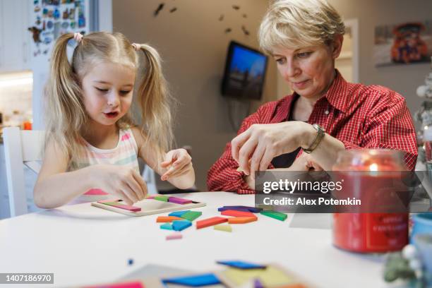 kleines mädchen, das mit ihrer großmutter am esstisch in der küche mit einem tangram-puzzle spielt. - tangram stock-fotos und bilder