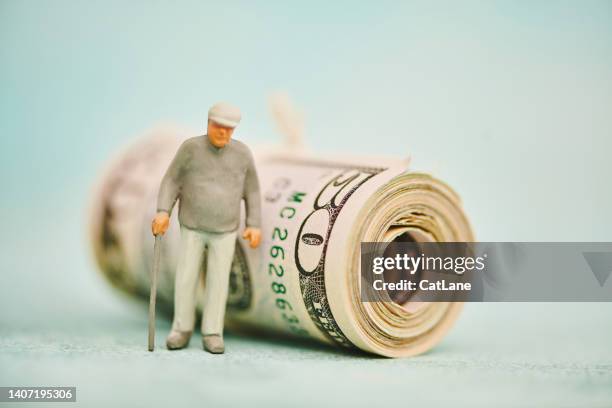 miniature figure of elderly man with walking stick next to a wad of fifty dollar bills - figurine bildbanksfoton och bilder