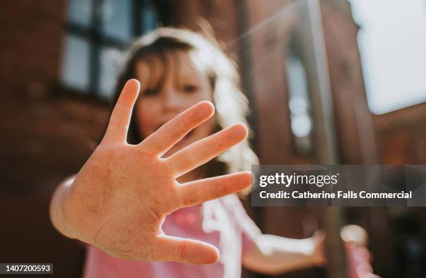 focus on a child's hand that is held towards the camera, fingers splayed, while the little girl remains in soft focus. - stretching fingers stock-fotos und bilder