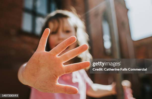 focus on a child's hand that is held towards the camera, fingers splayed, while the little girl remains in soft focus. - assertiveness stock pictures, royalty-free photos & images