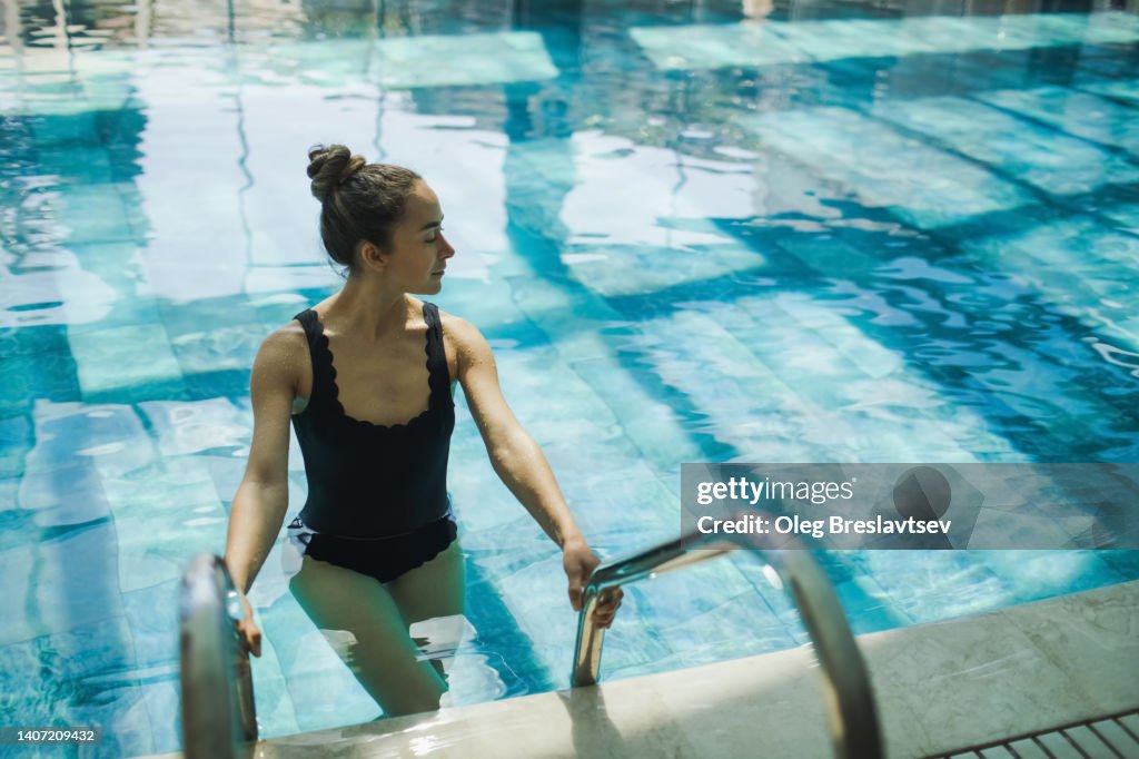 Woman going down in swimming pool and holding handrails. Female leisure and relaxation