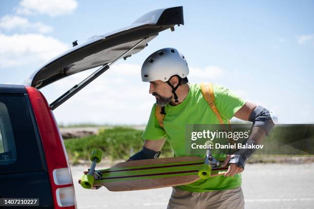 mature man with longboard returns to his car. - inserting imagens e fotografias de stock