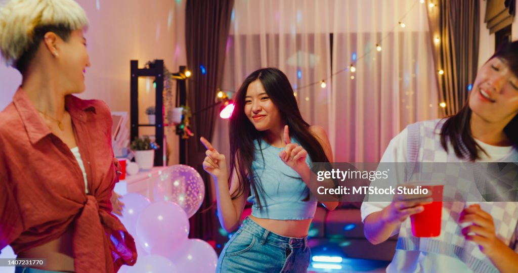 Junge asiatische Freundinnen, die tanzen und Spaß haben Spaß auf einer bunten Hausparty in der Nacht.