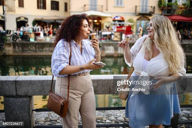 dos mujeres disfrutando de unas vacaciones de verano y comiendo un helado - navigli milano fotografías e imágenes de stock