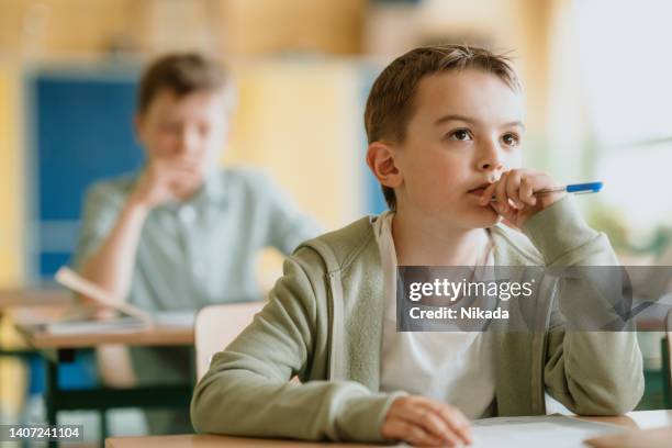 school boy with pen sitting in classroom - topics stock pictures, royalty-free photos & images